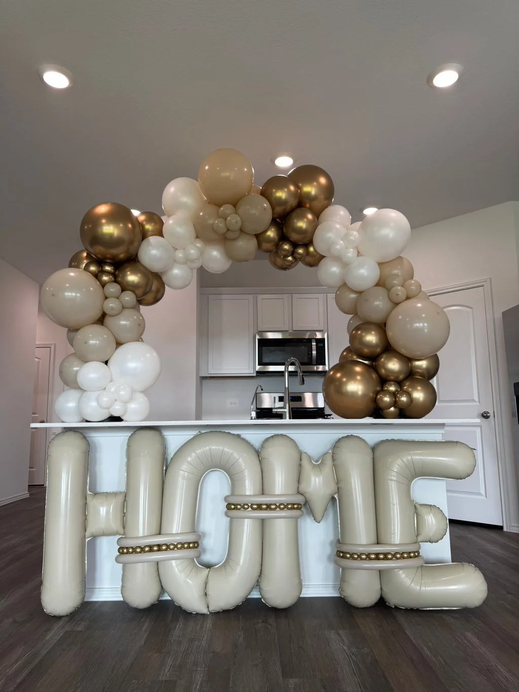 White, ivory and warm gold balloons form a rounded arch framing a bar opening above a LOVE display.
