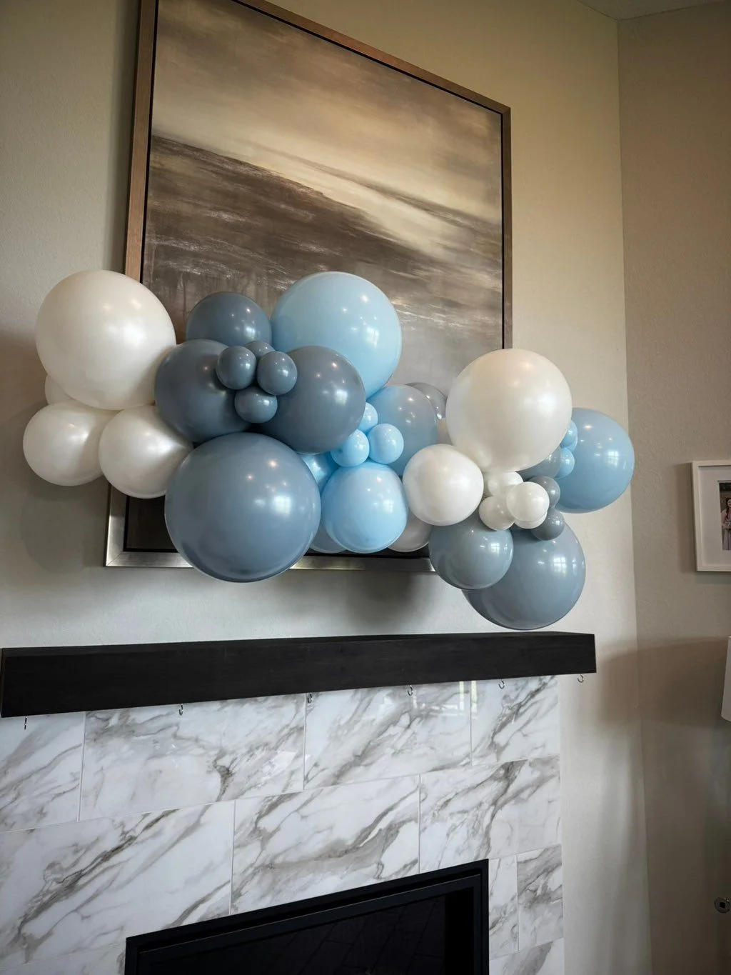 A free-form garland of ivory, pale blue and slate balloons arranged across a fireplace mantel.