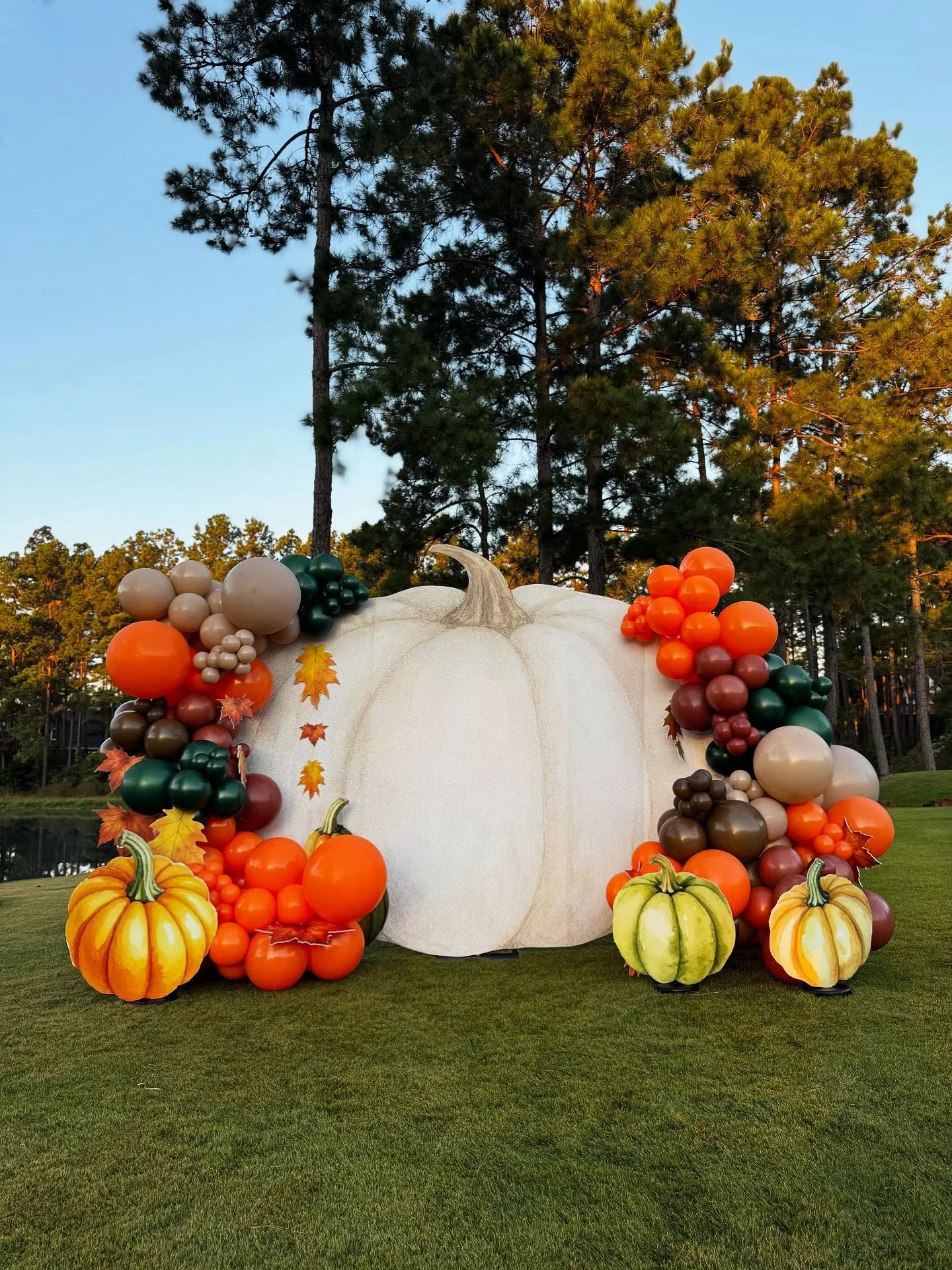 White pumpkin-shaped outdoor backdrop framed by orange, green and neutral balloon garlands and decorative pumpkins.