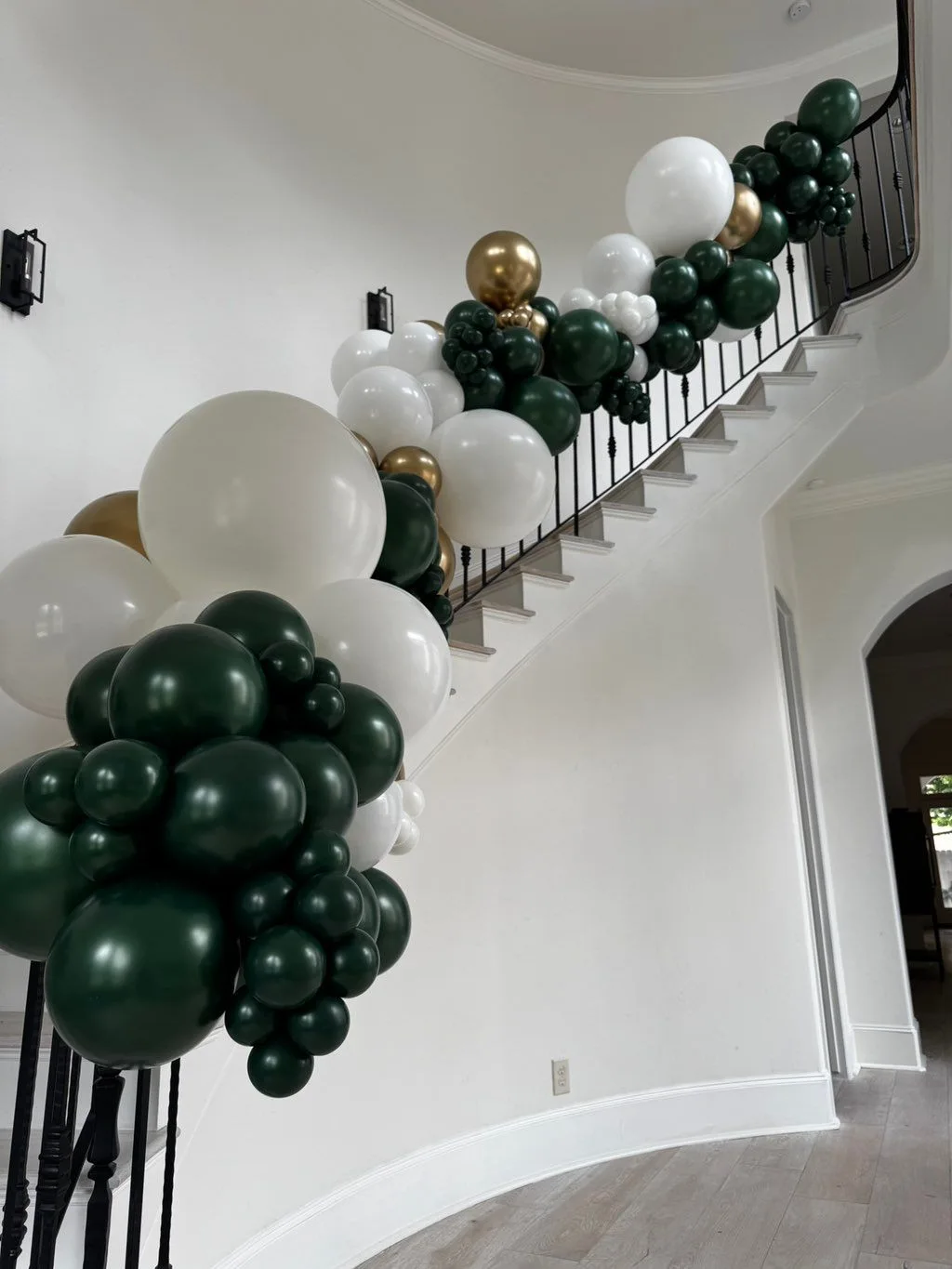 Deep green, white and gold balloon clusters follow an interior staircase railing.