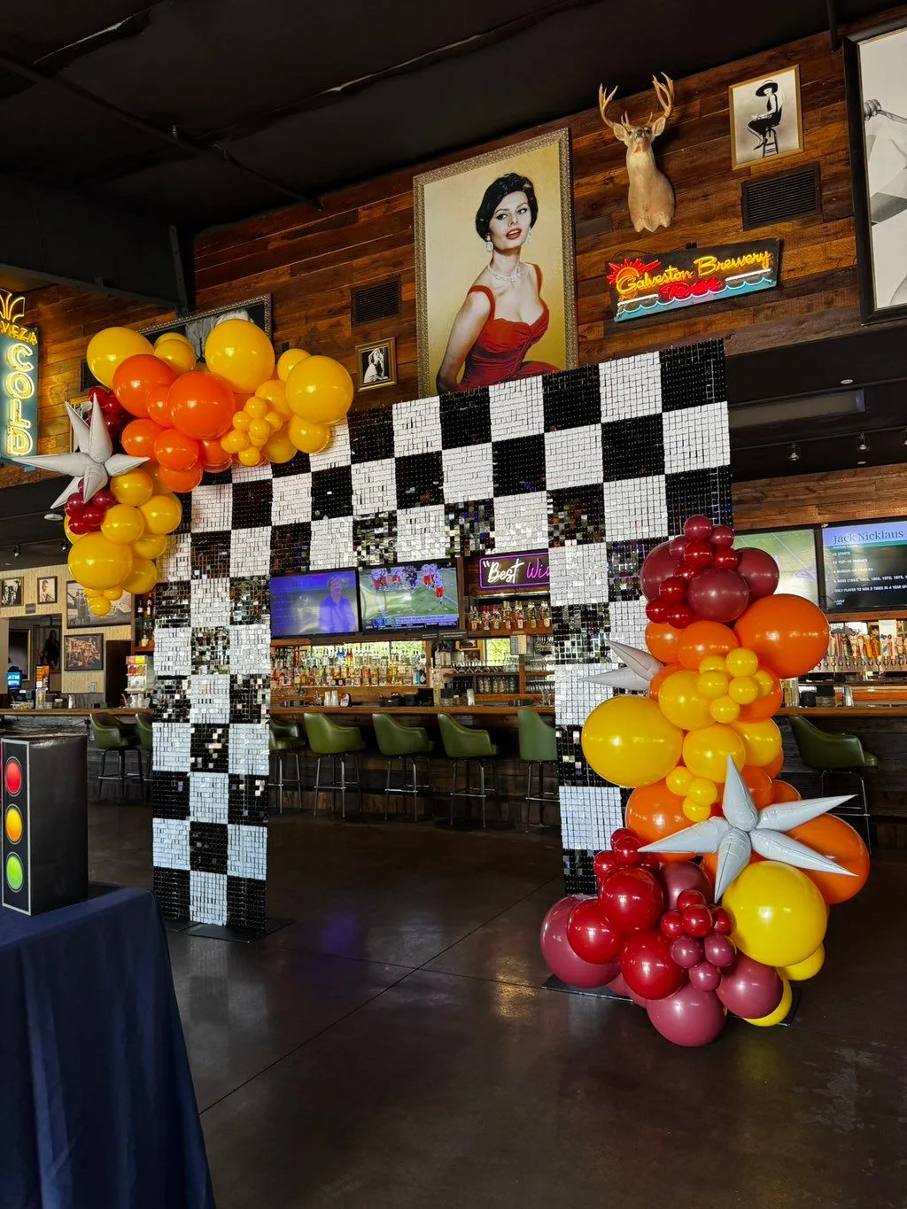 Red, orange and yellow balloons with silver accents frame a sparkling black-and-white checkered backdrop.